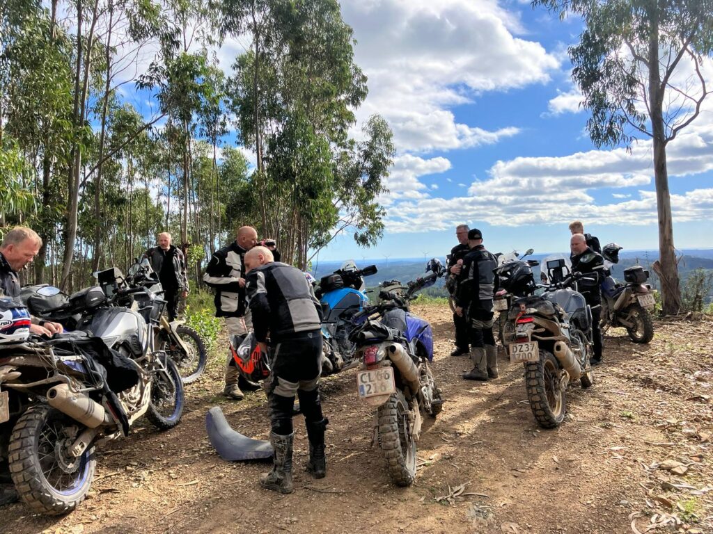 Mange motocykler og mennesker på toppen af et bjerg med blå himmel og træer.
